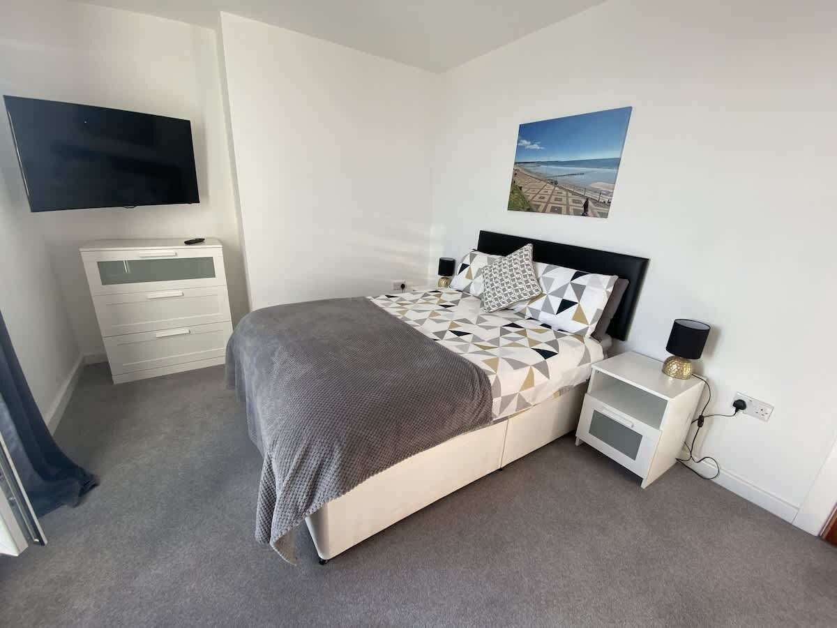 A bedroom with a bed, bedside tables, a TV, and a wall-mounted picture.