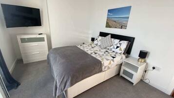A bedroom with a bed, bedside tables, a TV, and a wall-mounted picture.