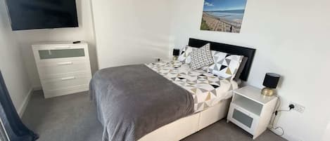 A bedroom with a bed, bedside tables, a TV, and a wall-mounted picture.