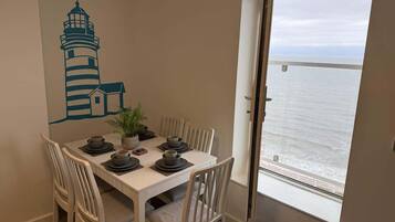A dining area with a table set for four, a potted plant, and a view of the sea through a large window.
