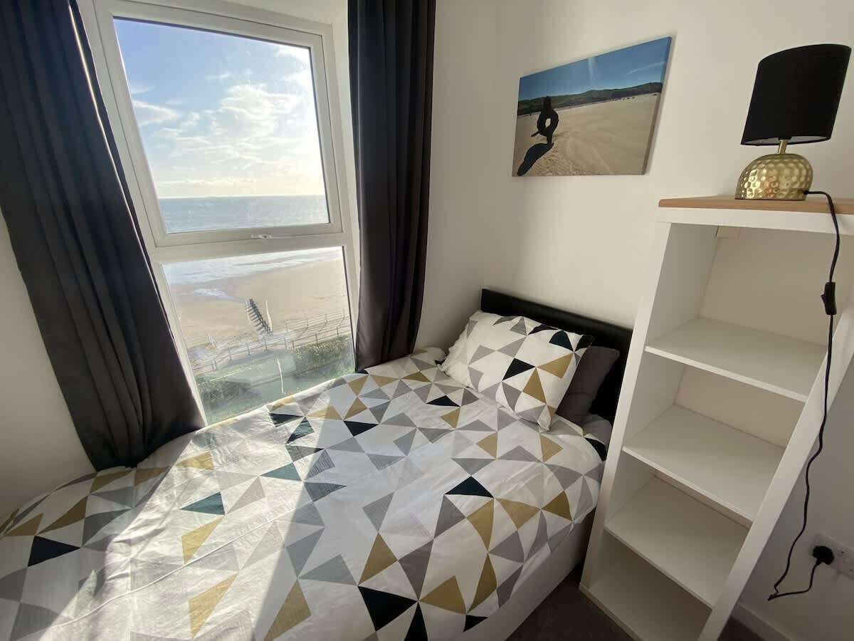 A bedroom with a bed, a window with curtains, a painting, and a lamp on a shelf.