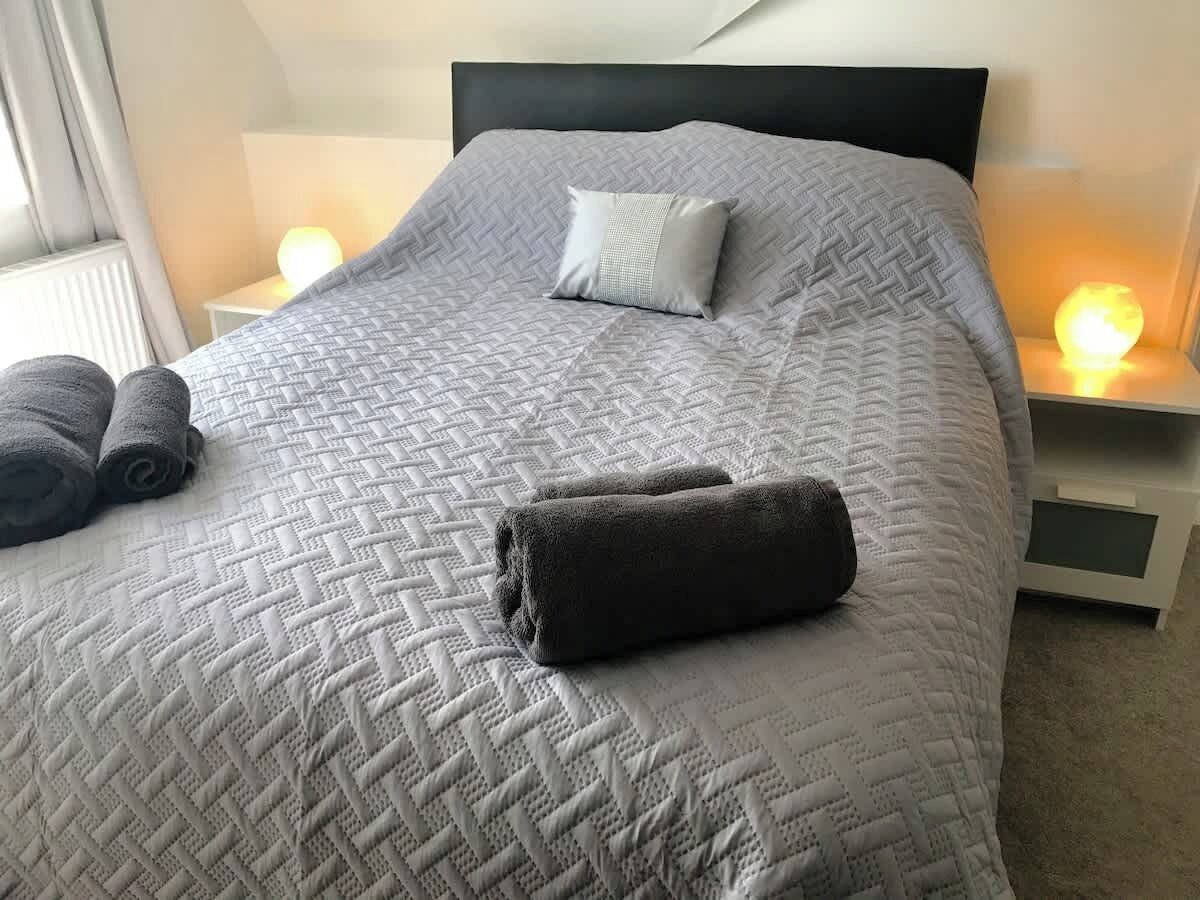 Una cama bien hecha con colcha acolchada, dos almohadas y toallas dobladas.