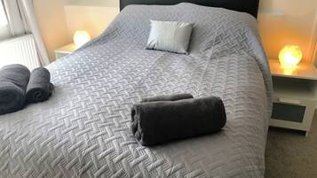 Una cama bien hecha con colcha acolchada, dos almohadas y toallas dobladas.