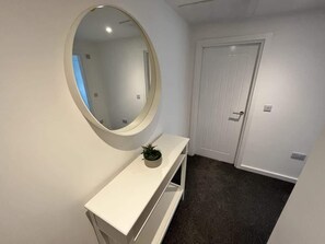 A hallway with a white door, a white console table with a mirror, and a small plant. - Seaside Escapes Apt. 5 (East Riding of Yorkshire)