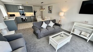 Ett modernt vardagsrum med en grå soffa, ett vitt soffbord och en tv som är monterad på väggen.
