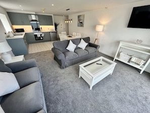 A modern living room with a grey sofa, a white coffee table, and a TV mounted on the wall. - Seaside Escapes Apt. 5 (East Riding of Yorkshire)