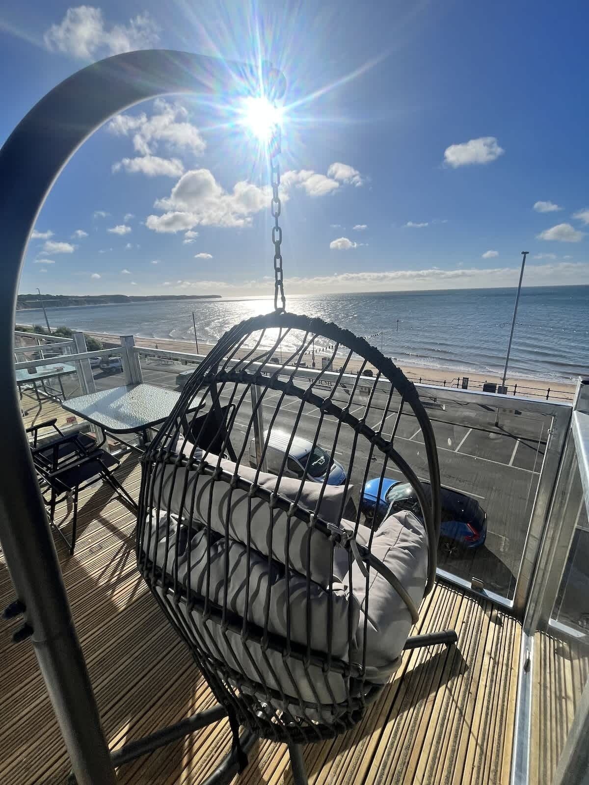 Terraza soleada con una silla colgante, vista al mar y un estacionamiento.