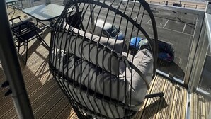 En solig terrass med en hängstol, utsikt över havet och en parkeringsplats.