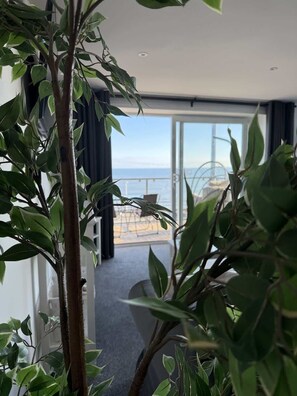 A room with a view of the sea, a balcony with a chair, and a plant in the foreground. - Seaside Escapes Apt. 5 (East Riding of Yorkshire)