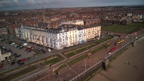 Ein großes, mehrgeschossiges Gebäude mit einem markanten Turm, umgeben von einem Parkplatz und einer Promenade.
