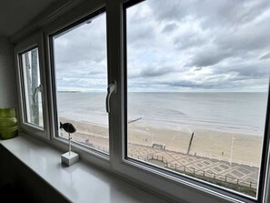 Blick aus einem Fenster auf einen Strand mit bewölktem Himmel.