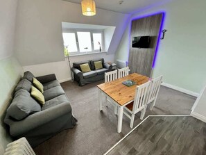 Ein modernes Wohnzimmer mit Sofa, Esstisch und Stühlen. Ein Fenster bietet einen Blick ins Freie.