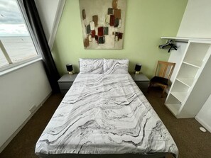 Ein Schlafzimmer mit einem Bett, einem Nachttisch, einem Stuhl, einem Regal und einem Fenster mit Blick.