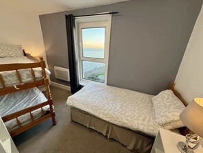 Ein Schlafzimmer mit Etagenbett, Einzelbett, Fenster mit Blick und Nachttischlampe.