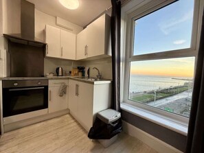 A compact kitchen with a view of the sea, a trash bin, and a window with curtains. - Fishermans Watch Apt. Oceana (East Riding of Yorkshire)
