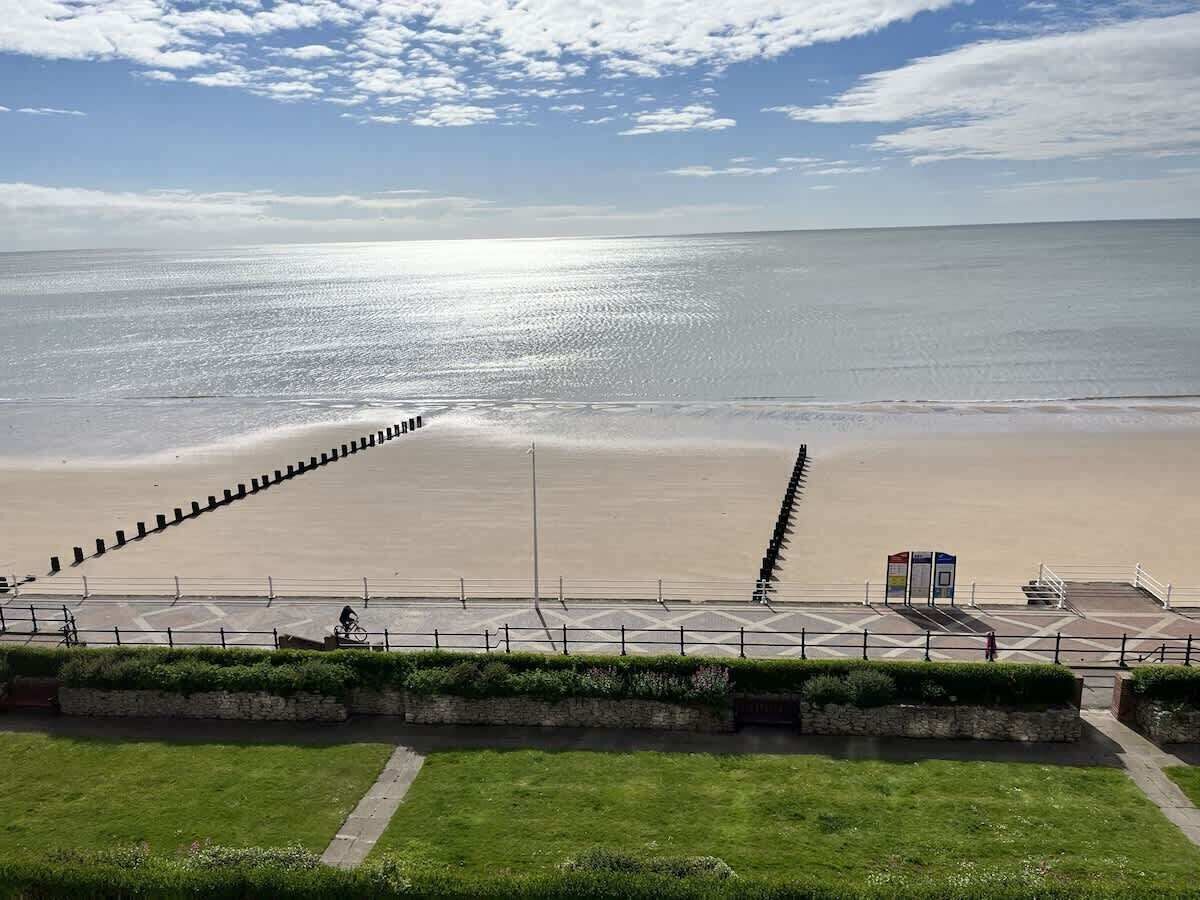 A coastal promenade with a walkway, a beach, and a clear sky.