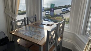 A dining table with a view of the sea and parking area through a window. - Promenade Apt. Oceana (East Riding of Yorkshire)