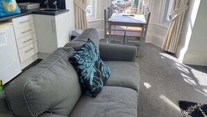 A living room with a sofa, a dining table, and a view of the outside. - Promenade Apt. Oceana (East Riding of Yorkshire)