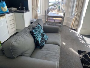 A living room with a sofa, a dining table, and a view of the outside. - Promenade Apt. Oceana (East Riding of Yorkshire)