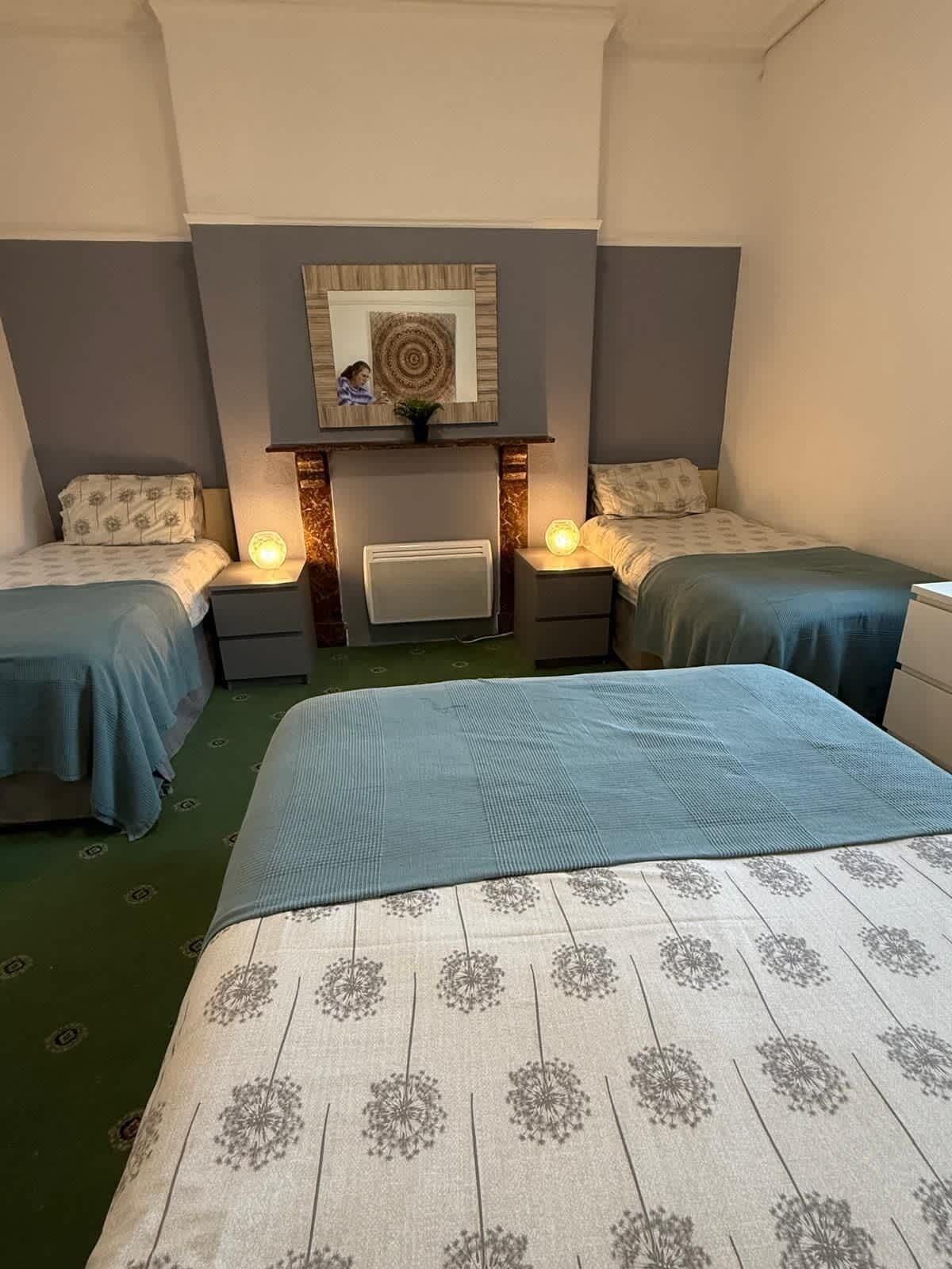 A hotel room with two single beds, a large bed, a mirror, and a wall-mounted artwork.