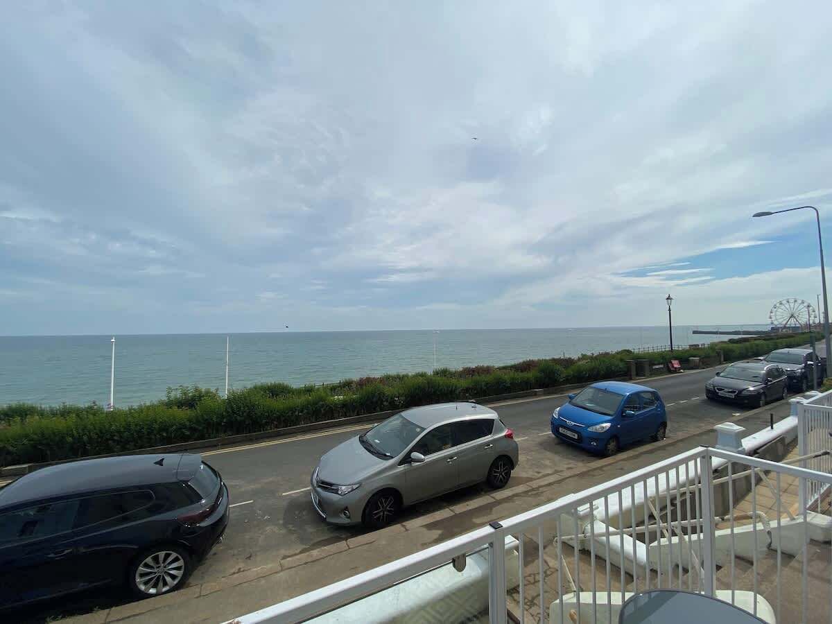 Eine Küstenstraße mit parkenden Autos, einem Riesenrad und freiem Blick auf das Meer.