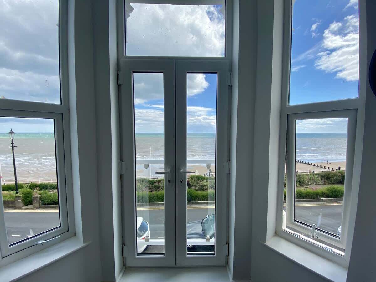 Blick durch ein Fenster auf einen Strand und das Meer im Hintergrund.