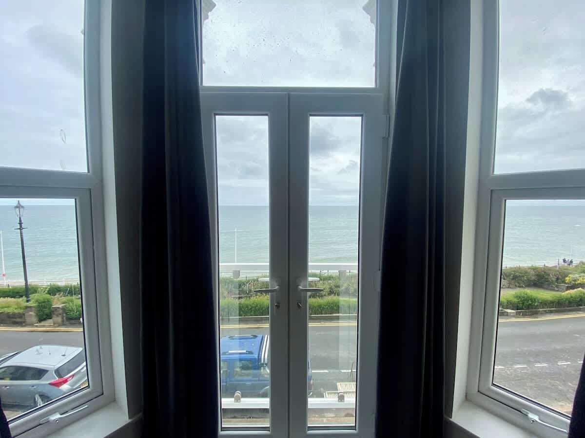 A view through a window with a view of the sea and a road with parked cars.