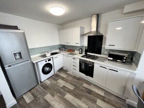 A compact kitchen with a refrigerator, washing machine, oven, microwave, and a stove. - 2 Bedroom Sea View Apartment with Balcony (Bridlington)