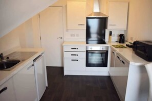 A compact kitchen with white cabinetry, a built-in oven, and a dishwasher. - 2 bedroom apartment, sea views, balcony & parking (Bridlington)