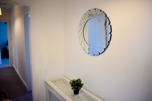 A hallway with a modern wall art piece and a small potted plant on a glass table. - 2 bedroom apartment, sea views, balcony & parking (Bridlington)