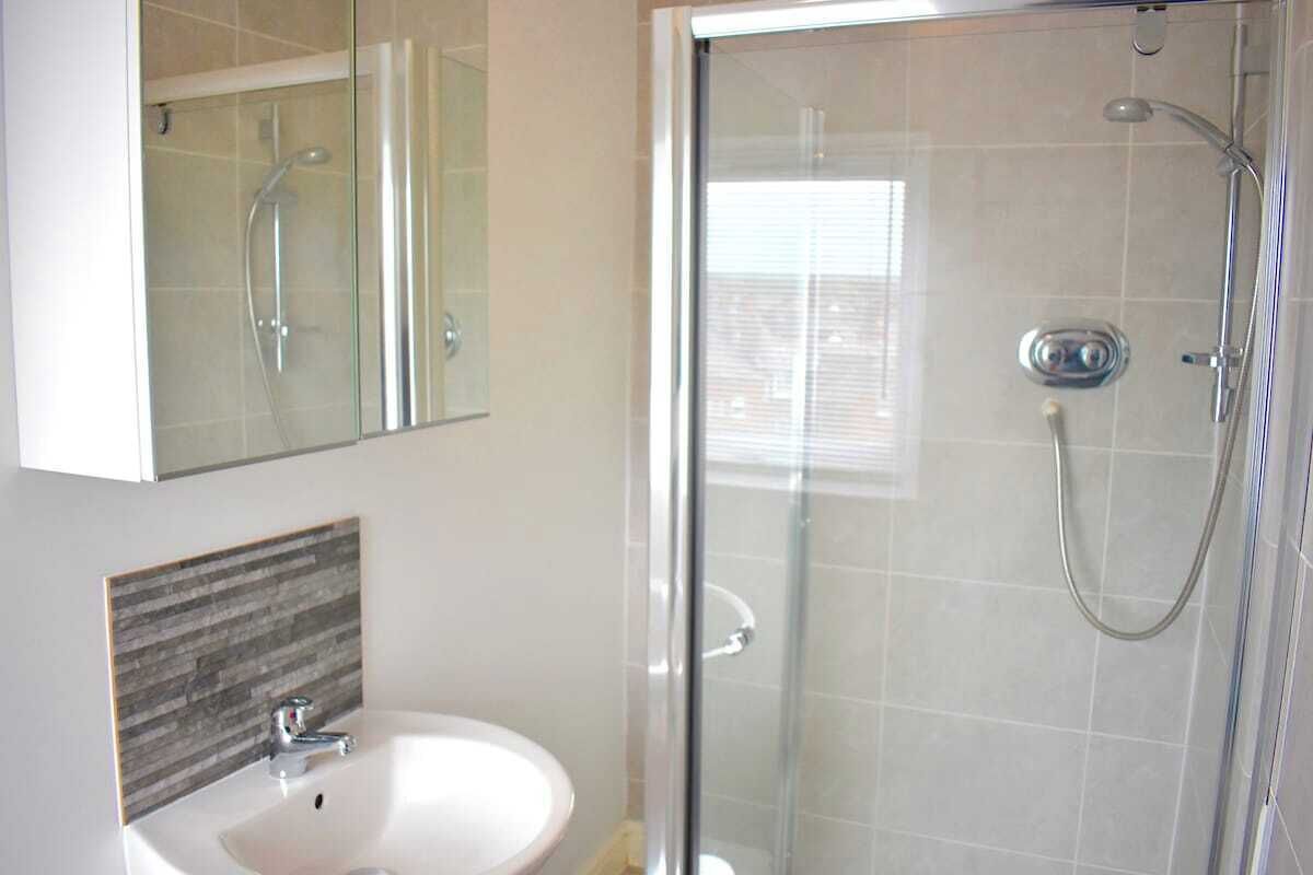 Un bany amb plat de dutxa de vidre, un lavabo blanc i un mirall sobre el lavabo.