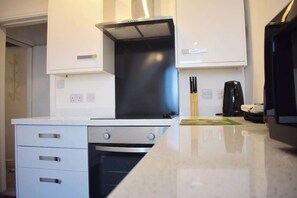A kitchen with white cabinets, a stainless steel oven, and a coffee maker on the counter. - 2 bedroom apartment, sea views, balcony & parking (Bridlington)