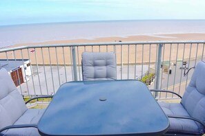 A balcony with a table and two chairs, overlooking a beach. - 2 bedroom apartment, sea views, balcony & parking (Bridlington)