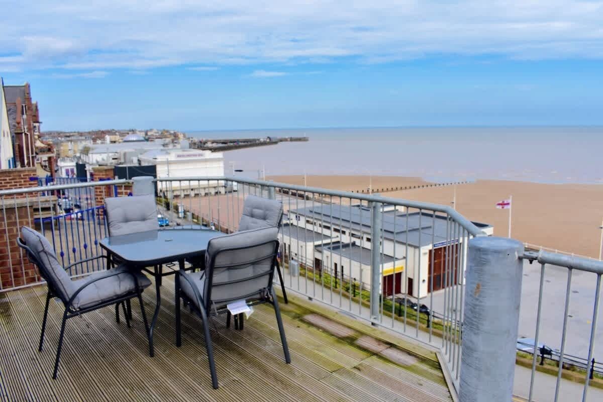 Un balcon avec une table et des chaises donnant sur une plage et une jetée.
