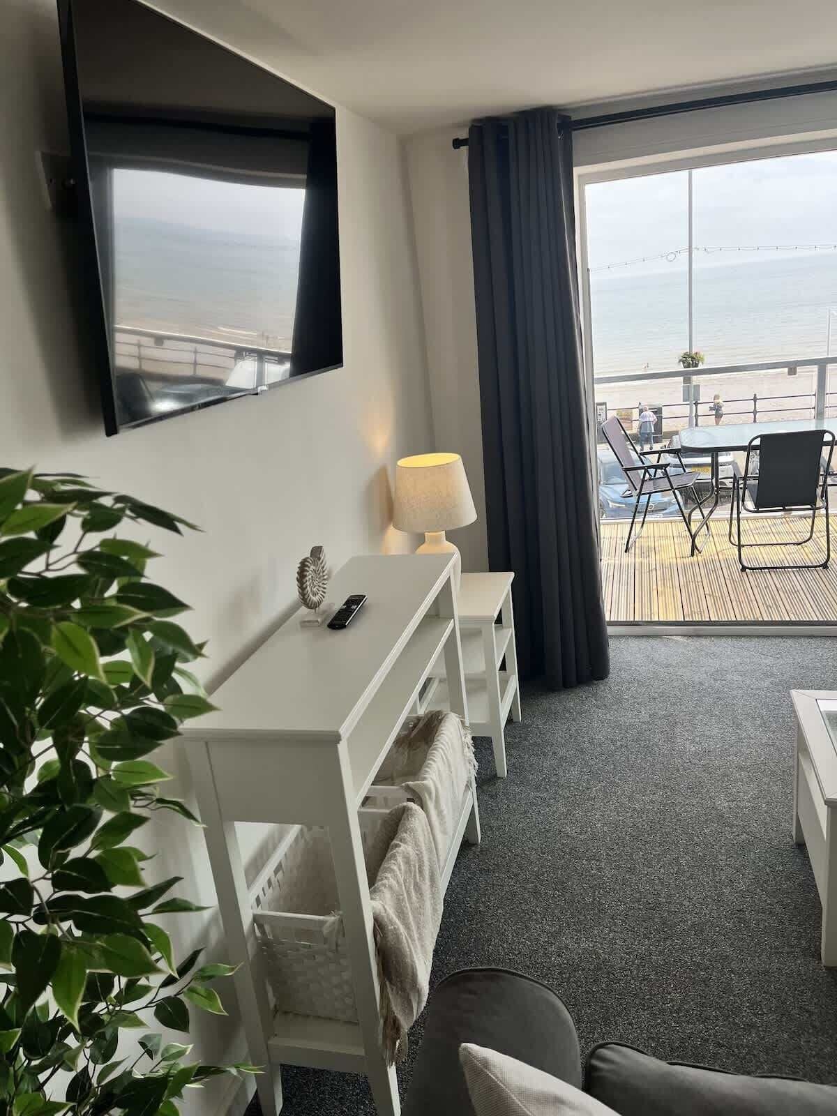 A hotel room with a balcony, a desk, a chair, a lamp, and a television.