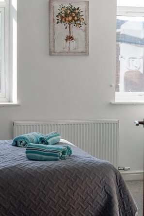 Ein Schlafzimmer mit Bett, Heizkörper, Fenster und einem Bild an der Wand.