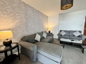 Ett vardagsrum med en grå soffa, ett soffbord, en lampa och tapeter med mönster.