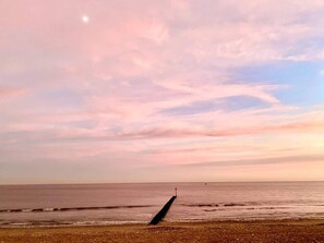 Ein Strand mit einem Steg, der sich ins Wasser erstreckt, bewölkter Himmel und ruhiges Meer.