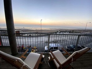 Ein Balkon mit Meerblick, ein Parkplatz und Liegestühle.