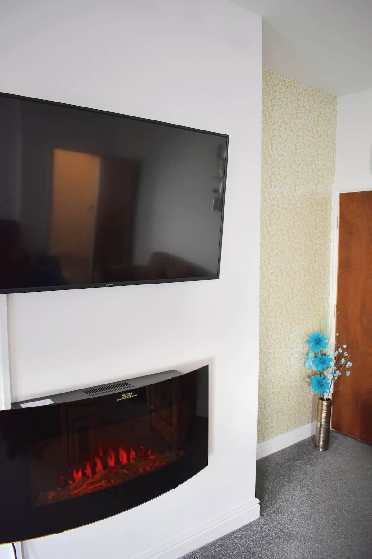 Ein Flachbildfernseher über einem Kamin mit sichtbarem Feuer.