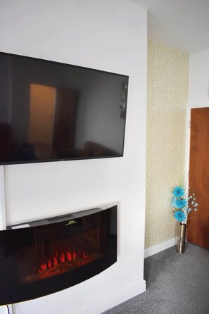 A flat-screen TV mounted above a fireplace with a visible fire. - Luxury 3 bedroom, sea view apartment with balcony (East Riding of Yorkshire)