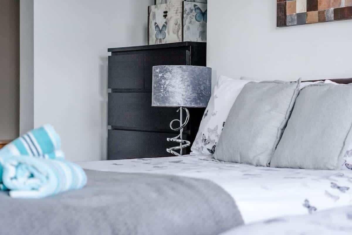 Et soveværelse med en seng, en mørk kommode, en lampe og en væg med kunstværker.