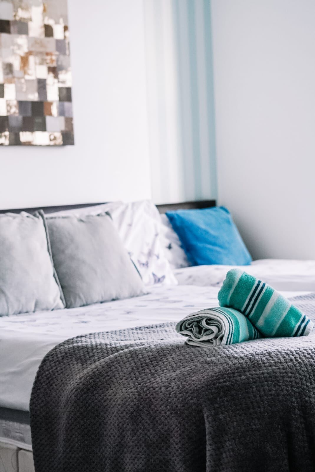 Un lit bien fait, avec un oreiller bleu, une couverture grise et une serviette verte à rayures posée sur le lit.