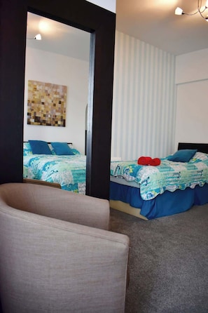 A bedroom with two beds, a large mirror, and a chair. - Luxury 3 bedroom, sea view apartment with balcony (East Riding of Yorkshire)