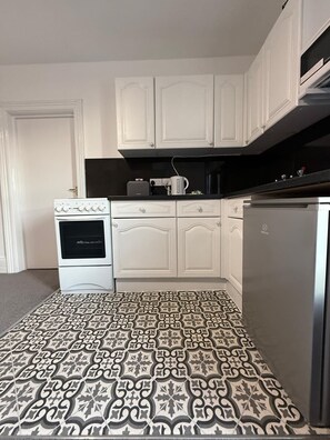 A kitchen with white cabinets, a stove, a microwave, and a refrigerator. - Ocean Wave Apt. Oceana (East Riding of Yorkshire)