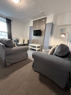 A modern living room with two grey sofas, a white coffee table, and a flat-screen TV mounted on a wooden panel wall. - Ocean Wave Apt. Oceana (East Riding of Yorkshire)