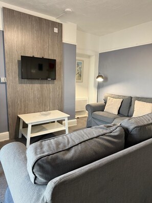 A living room with a grey sofa, a white coffee table, and a mounted TV. - Ocean Wave Apt. Oceana (East Riding of Yorkshire)