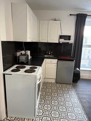 A compact kitchen with white cabinets, a microwave, a small refrigerator, and a stove. - Ocean Wave Apt. Oceana (East Riding of Yorkshire)