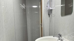 A bathroom with a white sink, a shower with a handheld showerhead, and a mirror on the wall. - Ocean Wave Apt. Oceana (East Riding of Yorkshire)