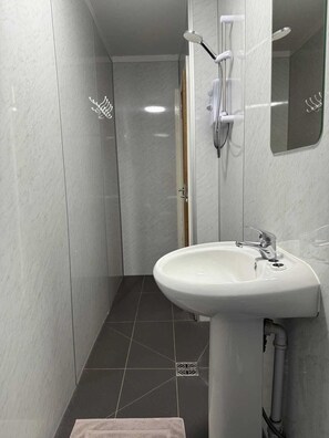 A bathroom with a white sink, a shower with a handheld showerhead, and a mirror on the wall. - Ocean Wave Apt. Oceana (East Riding of Yorkshire)